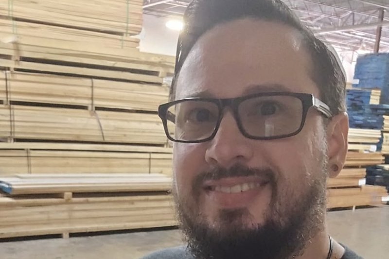 Michael Ownby smiling in the Brazos Forest Products warehouse, surrounded by stacked lumber
